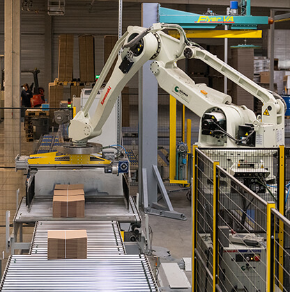 Ein Roboter verpackt eine fertige Verpackung aus Wellpappe. Danach liefern wir sie mit unserer eigenen Logistik zum Kunden.